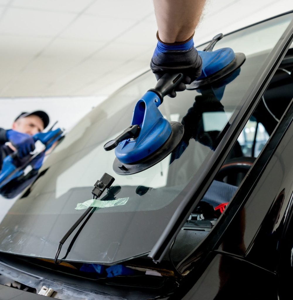 Automobile special workers replacing windscreen or windshield of a car in auto service station garage. Background